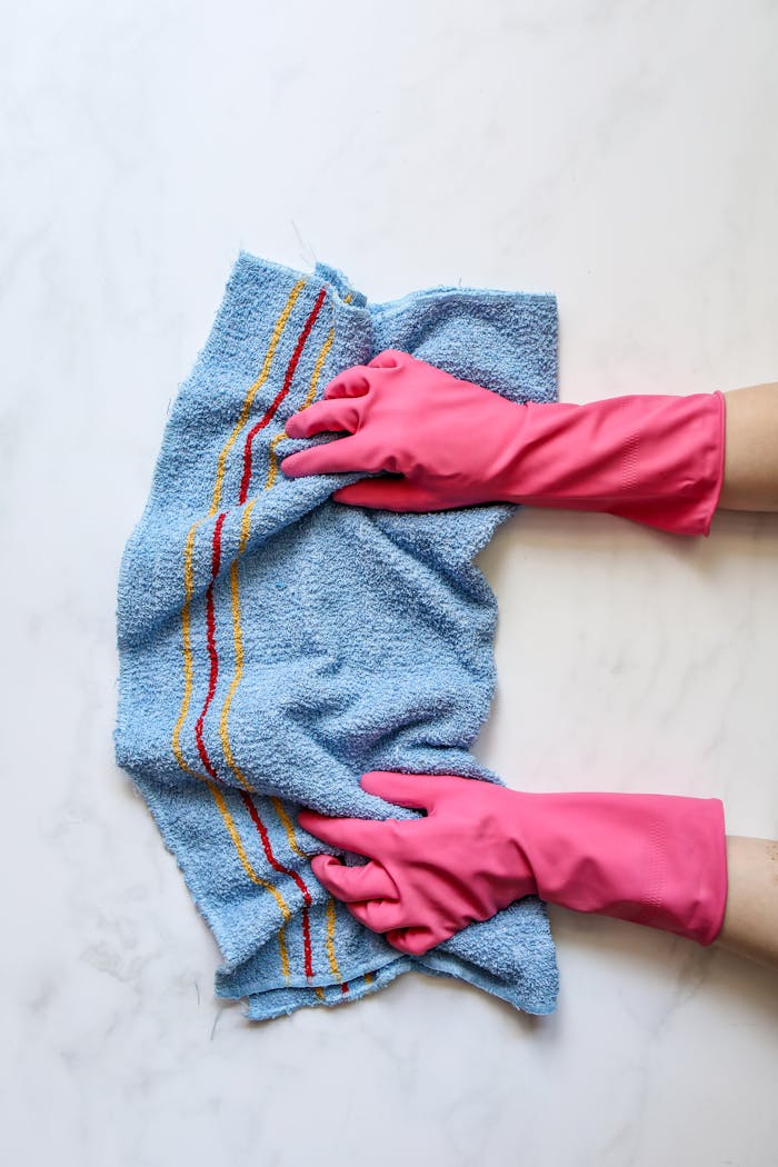 A person in pink gloves cleaning a marble surface with a blue cloth.